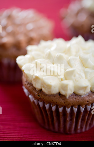 Lecker aussehende Schokolade Cupcake mit Vanille Zuckerguss auf eine rote Platzdeckchen-flacher Fokus Stockfoto