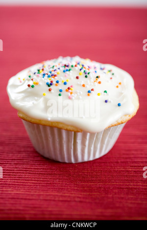 Delicious suchen Vanille Cupcake mit weißem Zuckerguss und Multi farbige Süßigkeiten auf rote farbige Ort mat - flachen Fokus Stockfoto