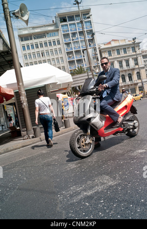 Ein Mann auf einem Moped in Athen hält in der Straße und schaut in Richtung der Kamera Stockfoto