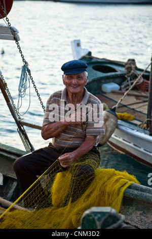 Ein alter Fischer flickt seine Netze auf seinem Boot im Hafen von Sami auf der Insel Kephalonia Stockfoto