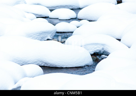 Bach fließt unter Felsbrocken mit Schnee bedeckt Stockfoto