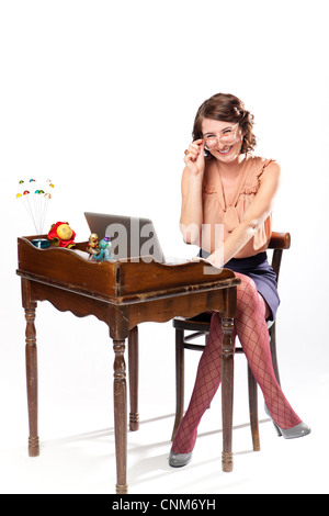 Eine Frau in Retro-Kleidung sitzt arbeiten an einem Vintage Schreibtisch lächelnd und hält ihre Brille. Stockfoto