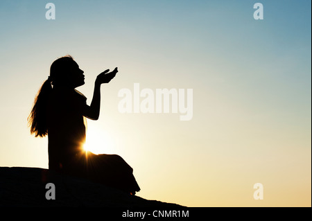 Indische Mädchen sitzen streckte ihre Hände bei Sonnenuntergang. Silhouette Stockfoto