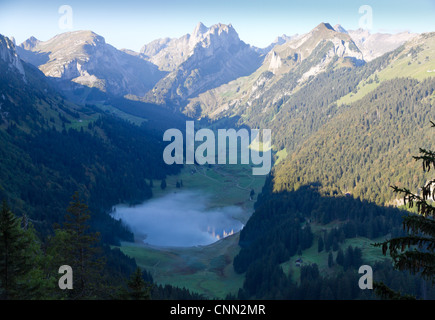 Tal mit See und Nebel schweben und Mountain peaks reflektierenden umgeben von hohen, steilen, felsigen Berg Wände am Säntis Stockfoto