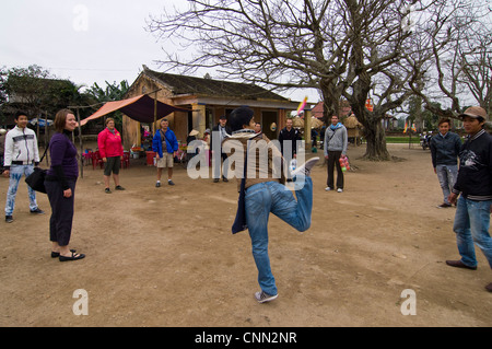 Horizontale Ansicht von Touristen mit vietnamesischen Einheimischen mit einem Spiel der Đá Cầu [Keepie Uppie] mit einem dekorativen Federball. Stockfoto