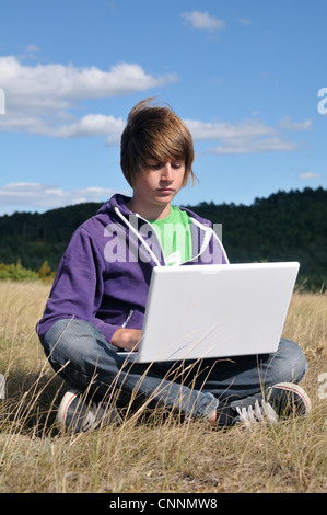 Junge sitzt im Feld mit Laptop-Computer, Blandas, Gard, Frankreich Stockfoto