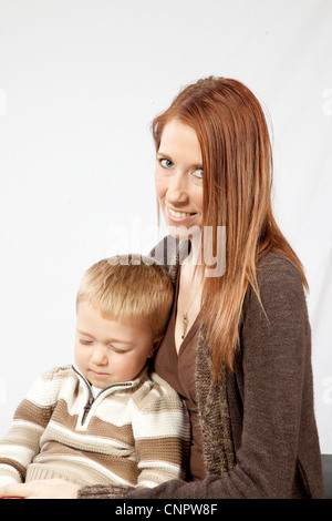 Hübsche Mutter mit roten Haaren, ihrem schlafenden blonden Sohn auf dem Schoß halten Stockfoto