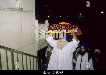 Sikh Mann trägt auf seinem Kopf Guru Granth Sahib, das Heilige Buch der Sikhs. Goldenen Tempel in Amritsar Stockfoto