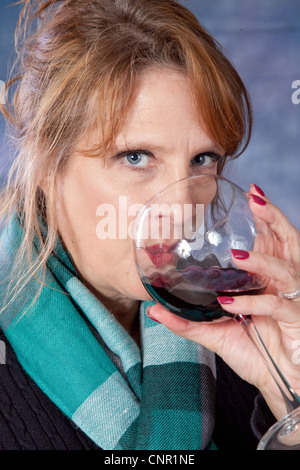 Schöne Reife Frau Glas Rotwein zu trinken und mit einem nachdenklichen Gesichtsausdruck in die Kamera schaut Stockfoto