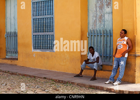 Alltag in Kuba - zwei einheimische, eine Stellung und einer Sitzung vor bunten Gebäude in Trinidad, Kuba Stockfoto