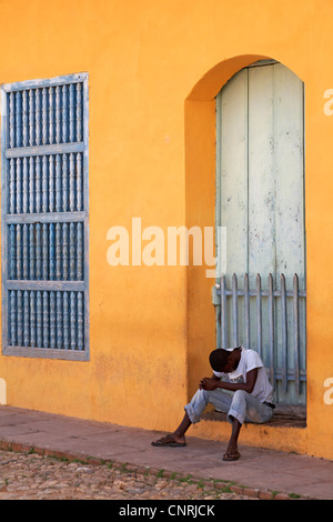 Alltag in Kuba - Afro-Karibischen Mann saß vor der bunten Gebäude blickte auf Trinidad, Kuba Stockfoto