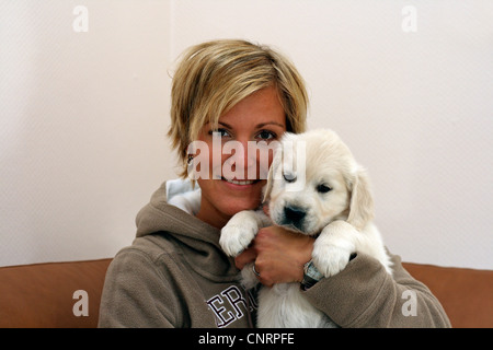 Golden Retriever (Canis Lupus F. Familiaris), junge Frau sitzt auf einem Sofa mit sechs Wochen alten Welpen auf dem arm Stockfoto