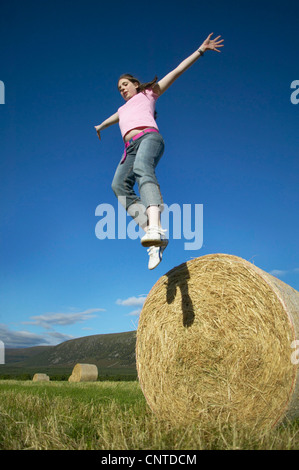 springen von einem Heuballen mit den armen Mädchen zu verbreiten, Großbritannien, Schottland, Cairngorm National Park Stockfoto