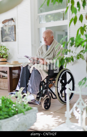 Älterer Mann im Rollstuhl lesen Stockfoto