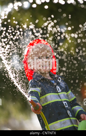 Junge in Feuerwehrmann Kostüm spielt mit Schlauch Stockfoto