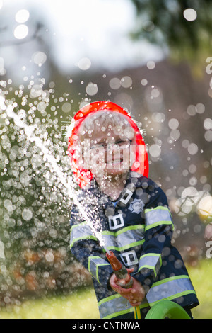 Junge in Feuerwehrmann Kostüm spielt mit Schlauch Stockfoto