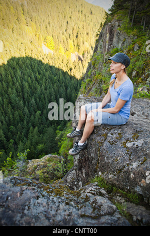 Eine Frau Wanderer sitzen am Rande eines Felswand nach oben auf einem Berg, Little Si Trail, Washington, USA. Stockfoto