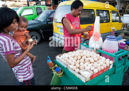 Frau mit ihrem Baby, kauft sie Balut, ein befruchtetes Ente Embryo von einem am Straßenrand Anbieter. Kohlenstoffmarkt, Cebu City, Philippinen Stockfoto