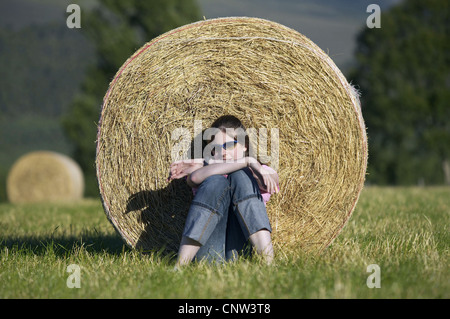 Junges Mädchen entspannend gegen Heuballen im Sommer, Großbritannien, Schottland, Cairngorm National Park Stockfoto