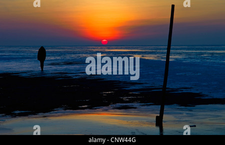Silhouette einer Frau stehend auf das Wattenmeer bei Ebbe mit Blick auf die Nordsee und den Sonnenuntergang, Cuxhaven, Landkreis Cuxhaven, Niedersachsen, Deutschland Stockfoto