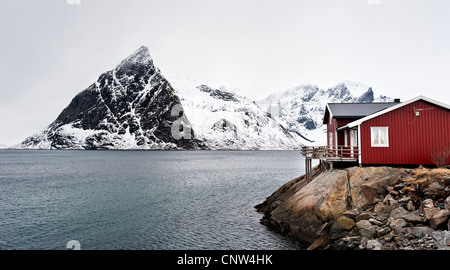 Eine Rorbu oder Fischer Hütte an der Küste in der Nähe von Hamnoy, mit Olstind Berg n Hintergrund Stockfoto