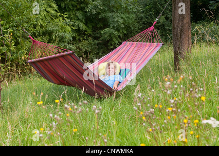 Mädchen liegen in der Hängematte aufgespannt zwischen Obstbäumen auf einer Wiese, Deutschland Stockfoto