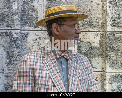 Ein dunkle älterer kubanischer Herr Stroh Strohhut Hut, aufgegebenes Anzug und Fliege zeichnet sich durch eine Steinmauer in Havanna. Stockfoto