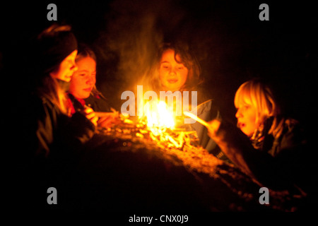 Kinder sitzen um ein Lagerfeuer am Abend, Deutschland Stockfoto