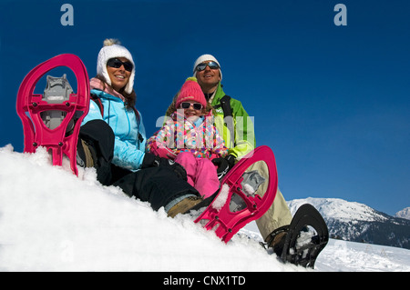 Familie mit drei sitzen im Schnee bei einer Neigung beim Schneeschuhwandern auf Urlaub in den Bergen, Frankreich Stockfoto