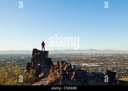 Eine Frau steht auf einem Felsvorsprung auf Piestewa Gipfel mit Blick auf Phoenix, Arizona / The Valley of The Sun. Stockfoto