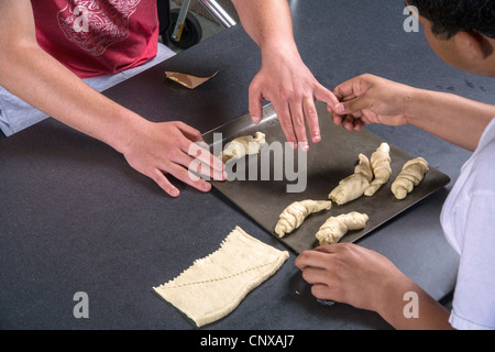 Ein Lehrer hilft einem behinderten Sehbehinderte Jugendliche machen durch Berührung von vorbereiteten Teig in einem Kochkurs rollt. Stockfoto