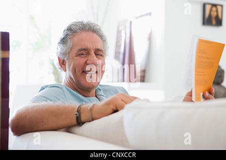 Ein fröhlicher senior Mensch zu Hause ein Buch zu lesen Stockfoto