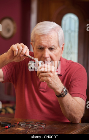 Ein Mann mit einer Pinzette auf einem Miniatur-Spielzeug-Motorroller Stockfoto