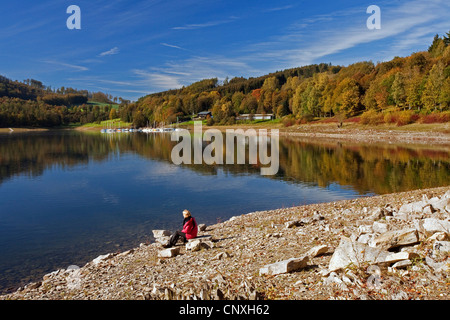 Frau am Seeufer von Henne Stausee sitzen und genießen Sie eine gute Aussicht, Meschede, Sauerland, Nordrhein-Westfalen, Deutschland Stockfoto