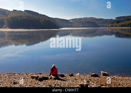 Frau am Seeufer von Henne Stausee sitzen und genießen Sie eine gute Aussicht, Meschede, Sauerland, Nordrhein-Westfalen, Deutschland Stockfoto