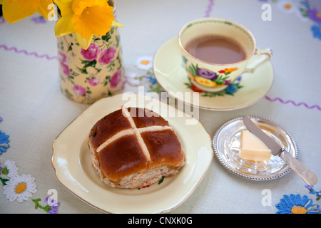 Ein heißes Kreuz Brötchen serviert auf einem Vintage China-Teller mit einer Tasse englischen Tee Stockfoto
