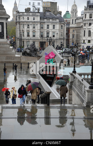 Trotz stürmischen Winden und Starkregen April besuchen Touristen Trafalgar Square und der Olympische Countdown-Uhr. Stockfoto