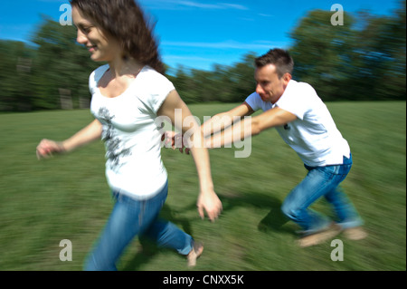 junges Paar läuft über eine Wiese herumalbern glücklich, Deutschland Stockfoto