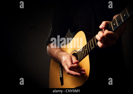 Man spielt eine akustische Gitarre in dunklen Umgebung Stockfoto