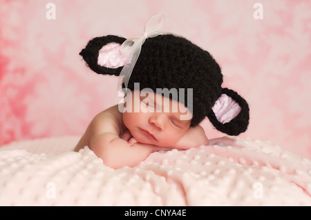 2 Wochen alten neugeborenen Mädchen trägt einen schwarzen gehäkelte schwarze Schafe Hut schlafen auf einer rosa Decke mit einem rosa Hintergrund. Stockfoto