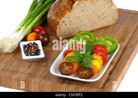 Einige Scheiben Bio-Tomaten in eine Schüssel mit einer Tasse mit Pfefferkörnern und Frühlingszwiebeln auf einem Bambus-Schneidebrett Stockfoto