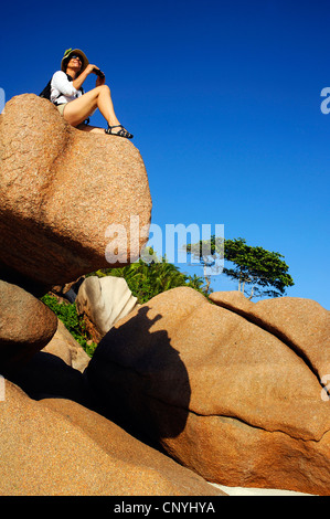 Frau sitzt auf Granitfelsen am Strand von Petite Anse, Seychellen, La Digue Stockfoto