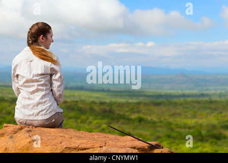 eine junge Frau auf einem Felsen sitzen und genießen Sie den Blick zum Savanne, Tansania, Tarangire National Park Stockfoto