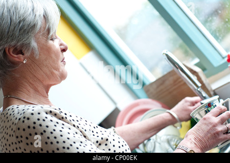 Mittlere gealterte Frau am Spülbecken in der Küche Stockfoto