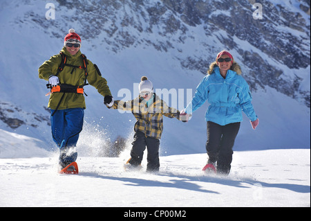 Familie im Winterurlaub gerne zu Fuß durch eine verschneite Berglandschaft hand in hand mit Schneeschuhen, Frankreich Stockfoto