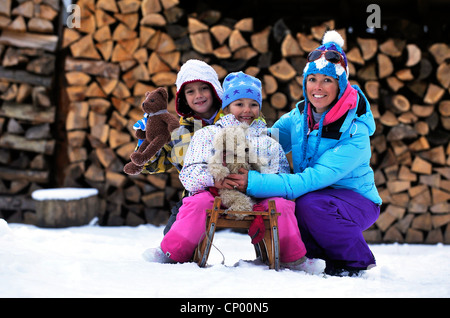 Mutter, hocken im Schnee neben ihrer beiden Söhne sitzen auf einem Schlitten mit ihren Teddy trägt in der hand, Frankreich Stockfoto