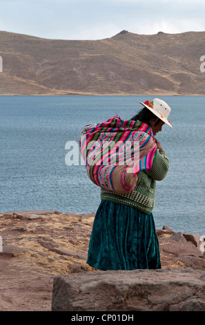 Quechua-Mutter mit einem Baby auf eine Decke auf der Rückseite am felsigen Seeufer, Peru, Atuncolla Stockfoto