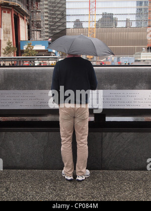 Touristen mit Regenschirm sieht in eines der Twin reflektierenden Pools in NYC 9/11 Memorial, 12. Oktober 2011, © Katharine Andriotis Stockfoto