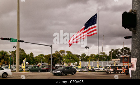 Große amerikanische Flagge weht im Wind über einen Auto-Vorplatz auf einer großen Straßenkreuzung in Miami. Stockfoto