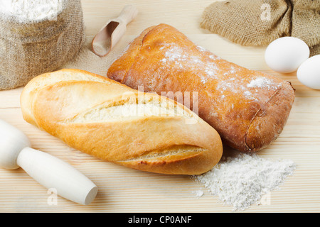Frisch gebackenes Baguette und Brot auf Holzbrett, Mehlsack, Nudelholz Stockfoto